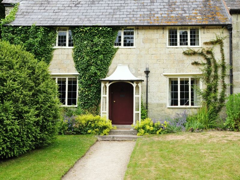 A stone cottage with a porch, climbing plants and a garden path