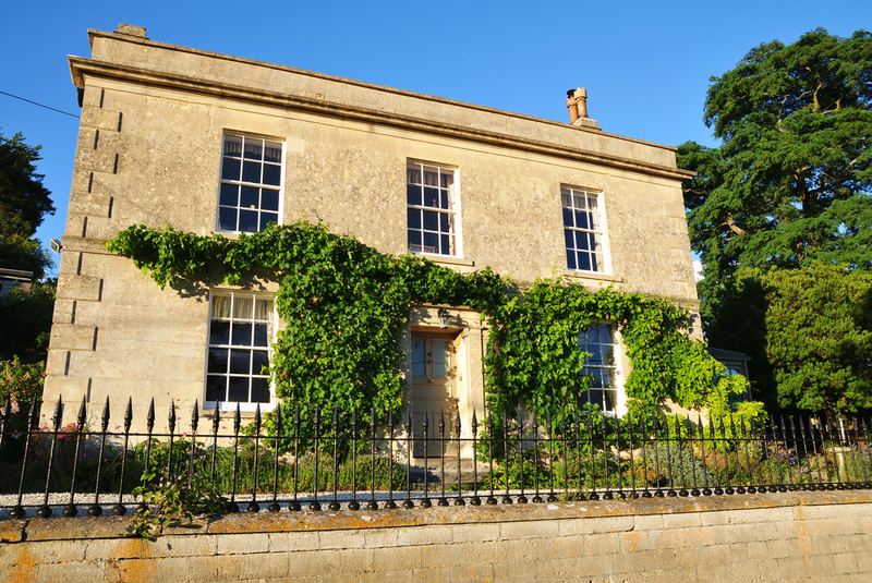 A Georgian stone house with climbing plants, behind iron railings