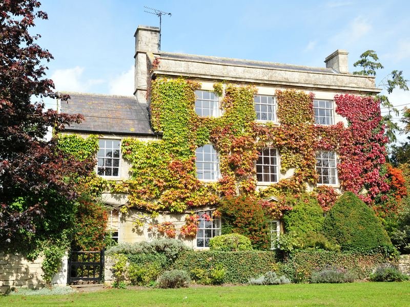 A stone house covered in red and green climbing plants