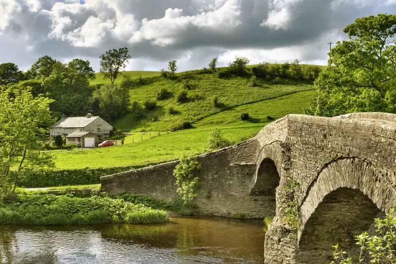 An old stone bridge over a river, with a cottage beyond