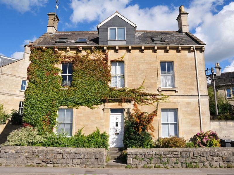 A three-storey stone house with climbing plants, behind a stone wall